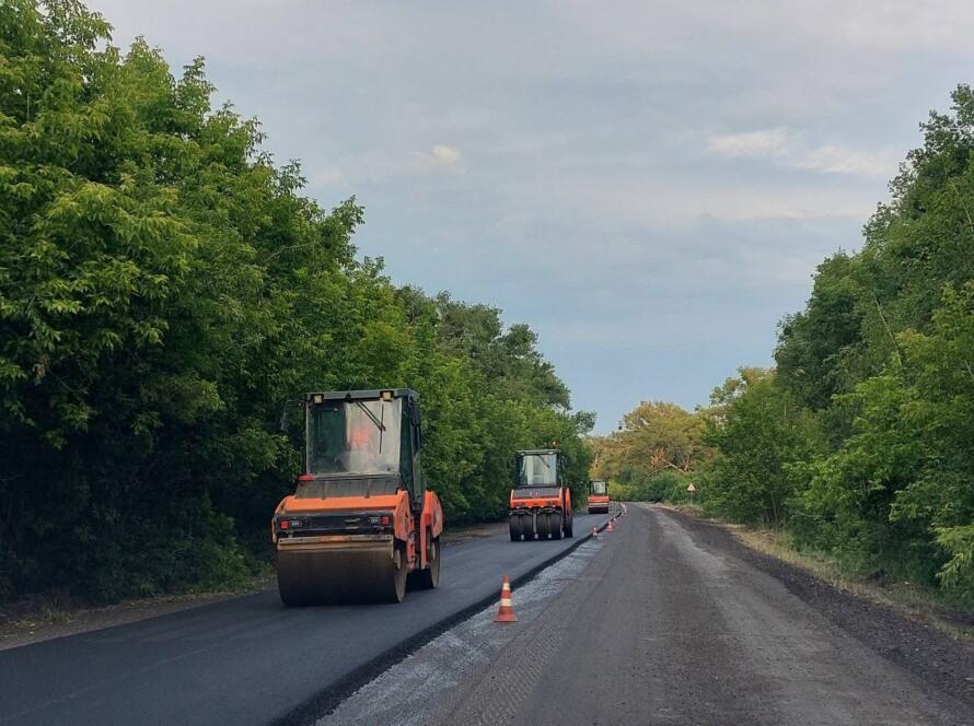 Асфальтувальні котки працюють на оновленні дорожнього покриття серед зелених насаджень